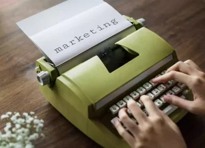 Grüne Schreibmaschine mit einem Blatt, auf dem das Wort marketing geschrieben ist.